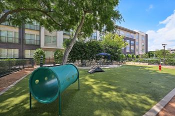 A playground with a green slide and a tent in the background at Everra Midtown Park Apartments, Dallas, Texas